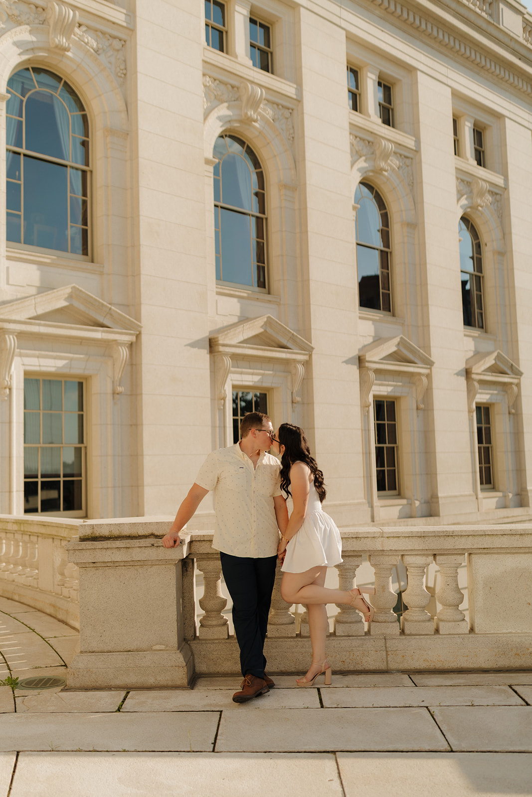 Elegant engagement moment with a couple kissing in front of a historic building, full of sweet energy.