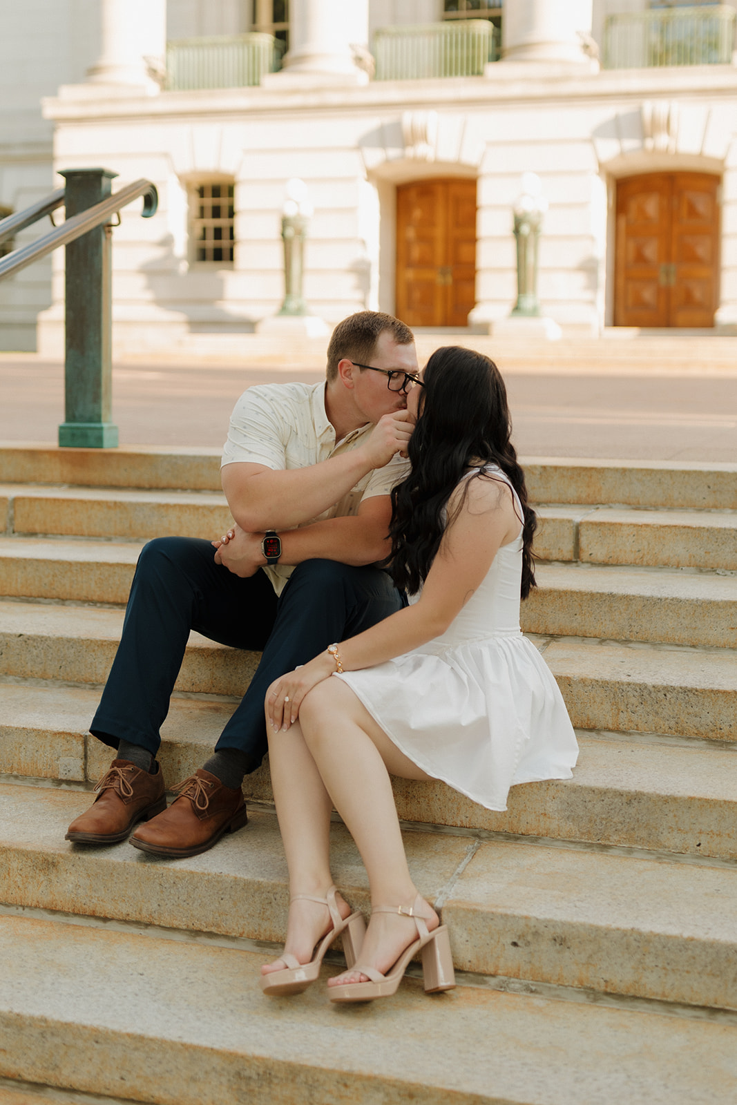 Classic engagement moment with a couple kissing on stone steps in front of a courthouse.
