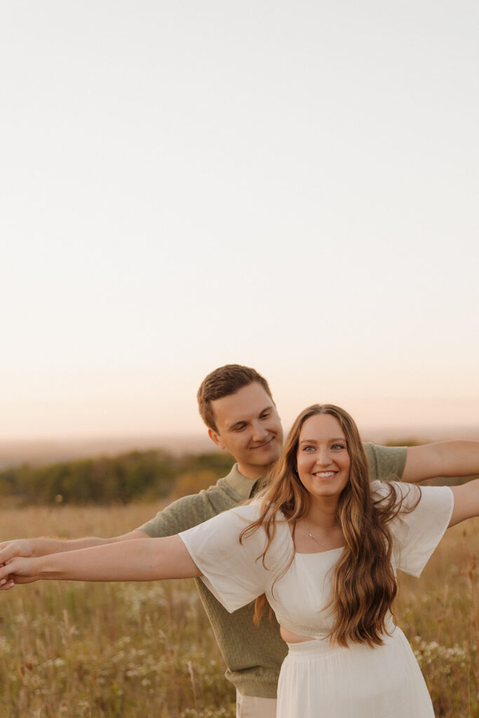Joyful outdoor engagement photos of a couple laughing together in a wildflower field at sunset.

