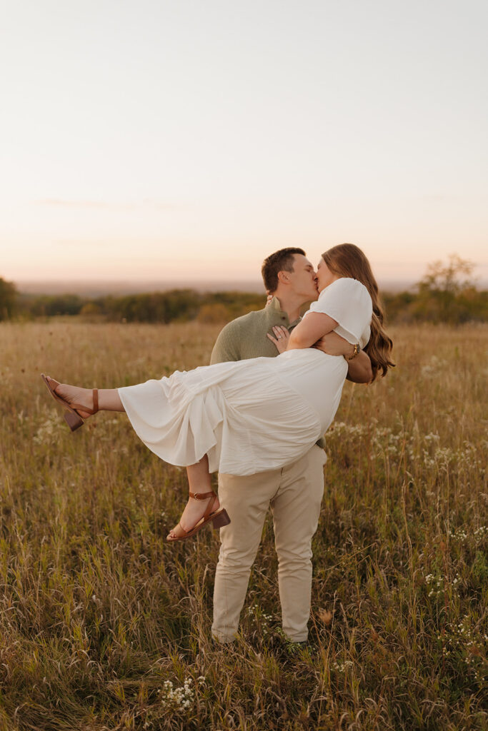 Golden hour outdoor engagement photos with a couple kissing in a wildflower field, full of movement and joy.