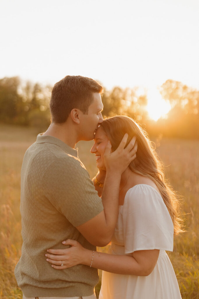 Tender golden hour moment with a couple embracing and smiling in a warm field of tall grass.