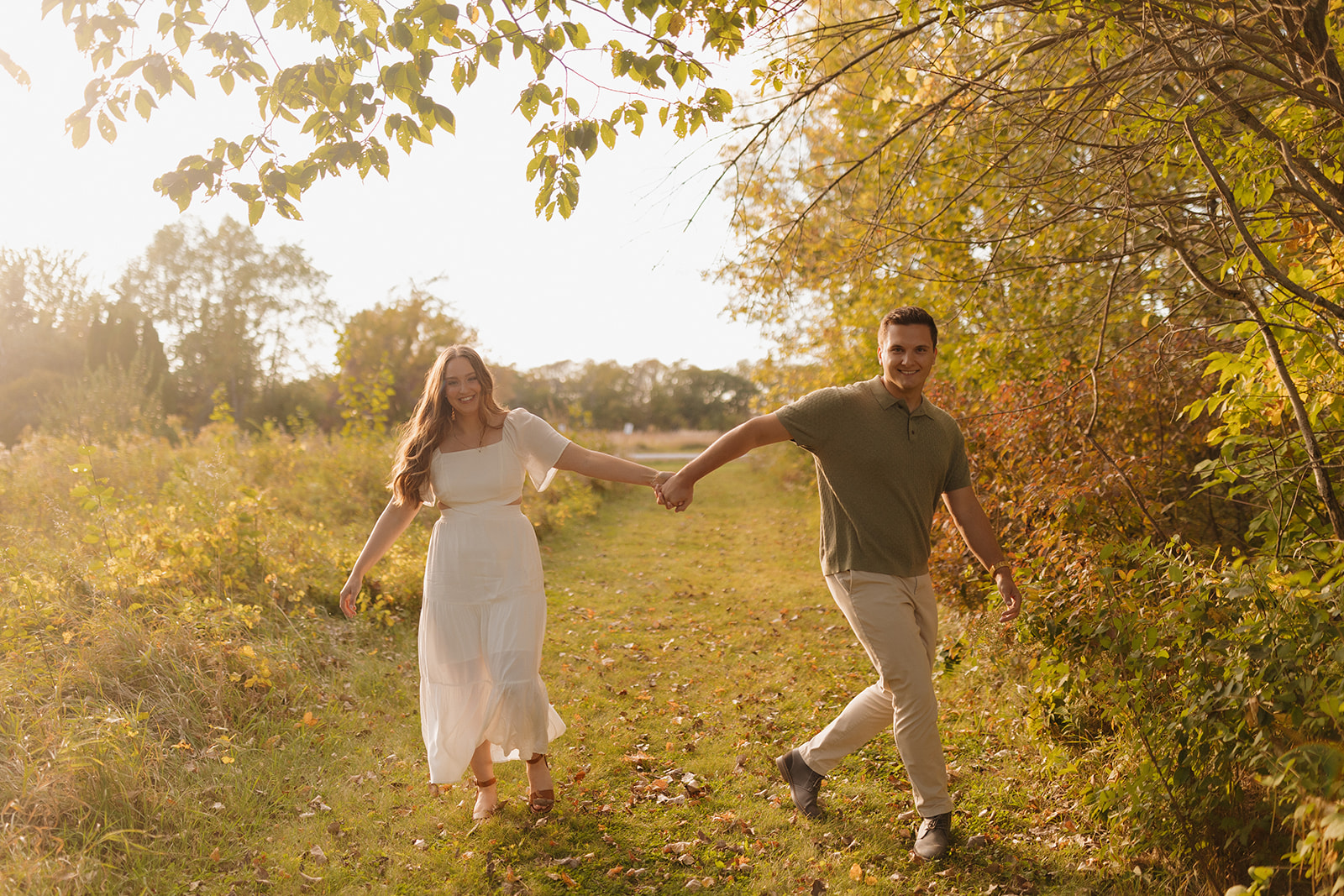 Candid outdoor engagement photos of a couple walking hand in hand through a sunlit forest path.