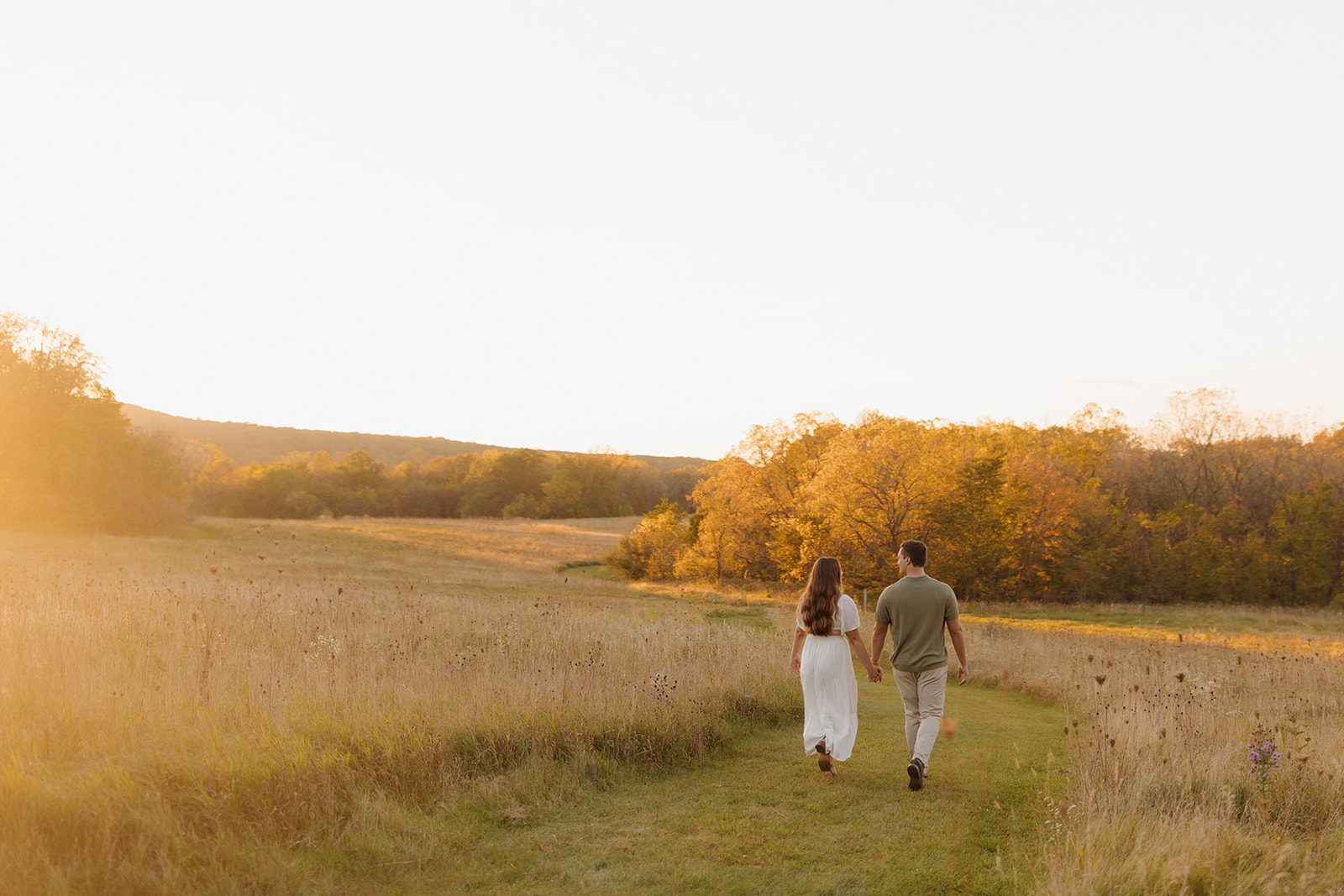 Dreamy outdoor engagement photos of a couple strolling through a golden field at sunset.