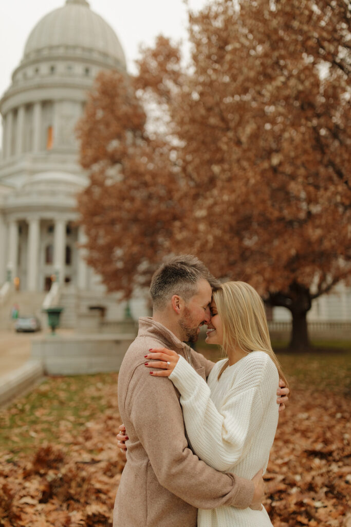 Cozy autumn engagement session with a couple embracing near the Wisconsin Capitol building.
