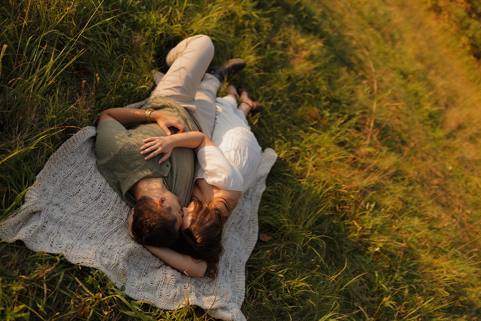 Dreamy outdoor engagement photos of a couple lying together in the grass, wrapped in golden light.

