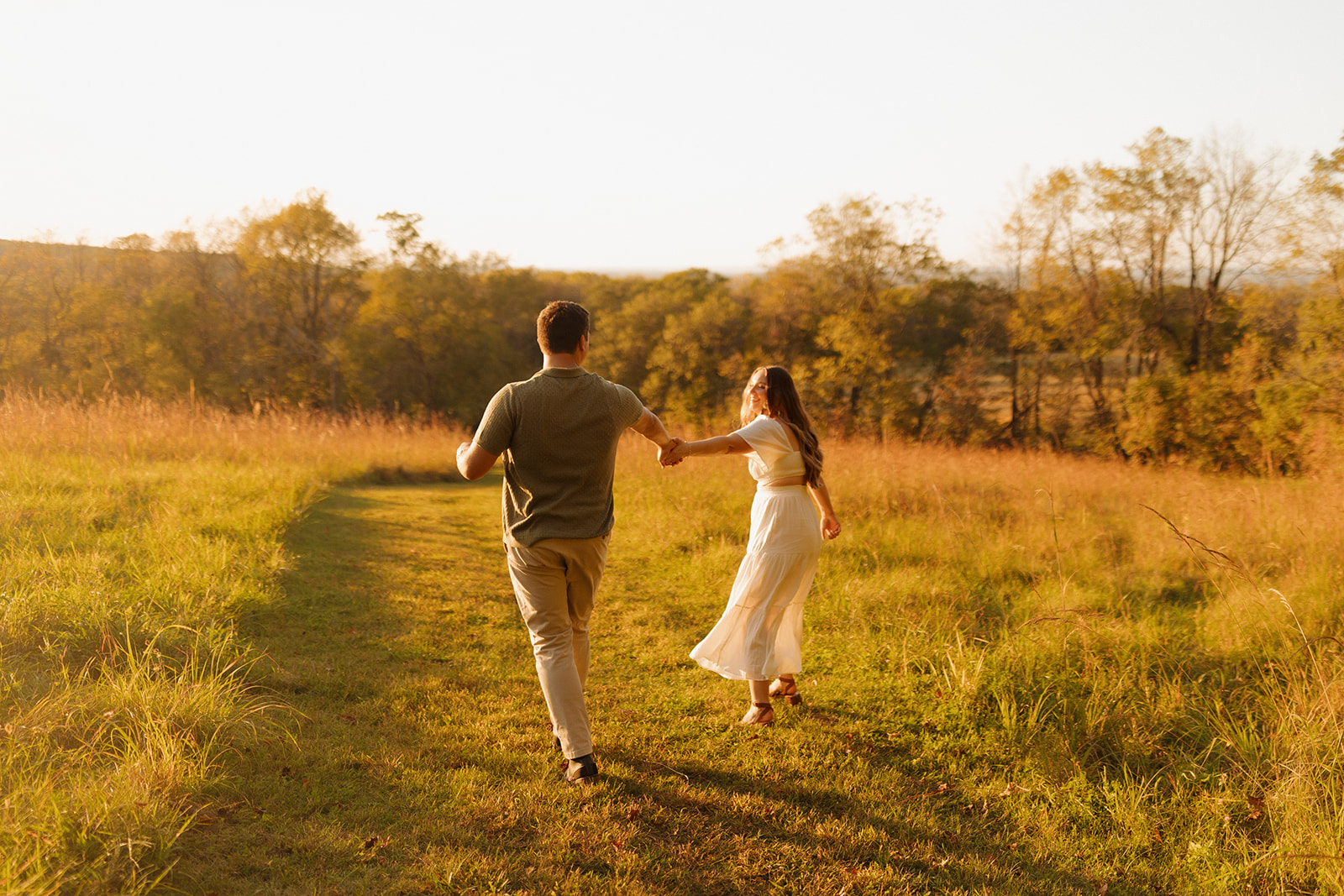 Playful outdoor engagement photos of a couple running hand-in-hand through a glowing Wisconsin meadow.

