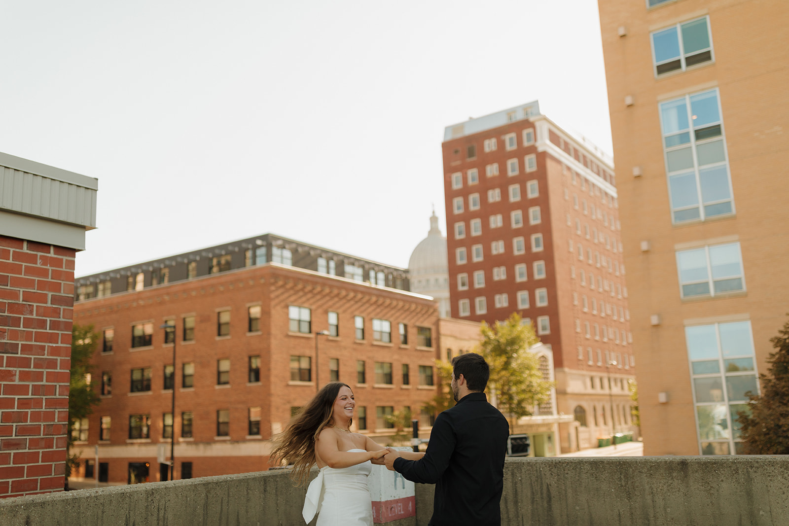 Outdoor engagement photos of a couple holding hands and dancing on a downtown rooftop with the Capitol dome in the distance.