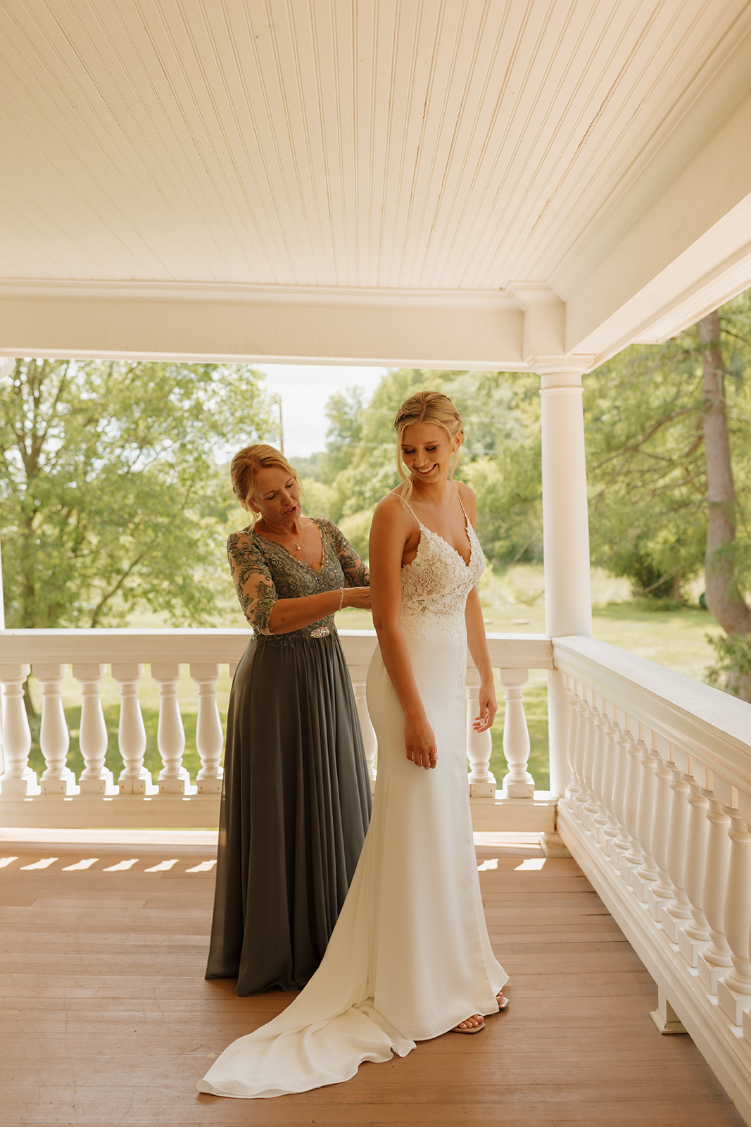 Bride's mother helping button her in her wedding dress on rustic porch before outdoor wedding ideas come to life at her Wisconsin wedding