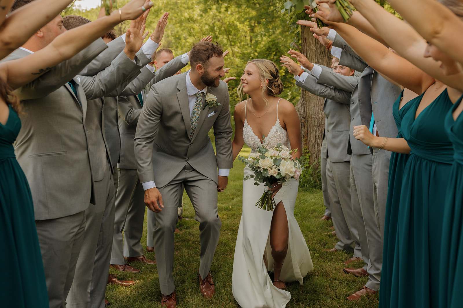 Bride and groom look at one another in excitement celebrating recent marriage while walking through tunnel of hands by wedding party