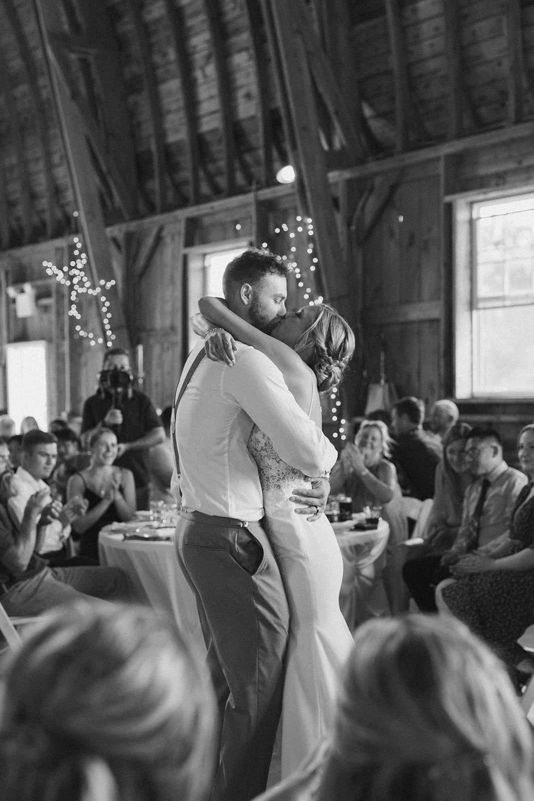 Romantic and candid moment of newly married couple during first dance in barn with lights and guests 