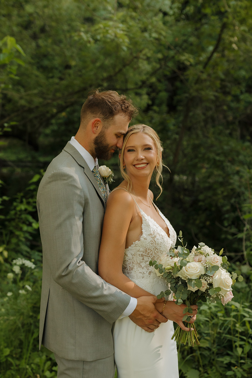 Bride smiles as groom hugs her from behind after outdoor wedding celebration in Wisconsin