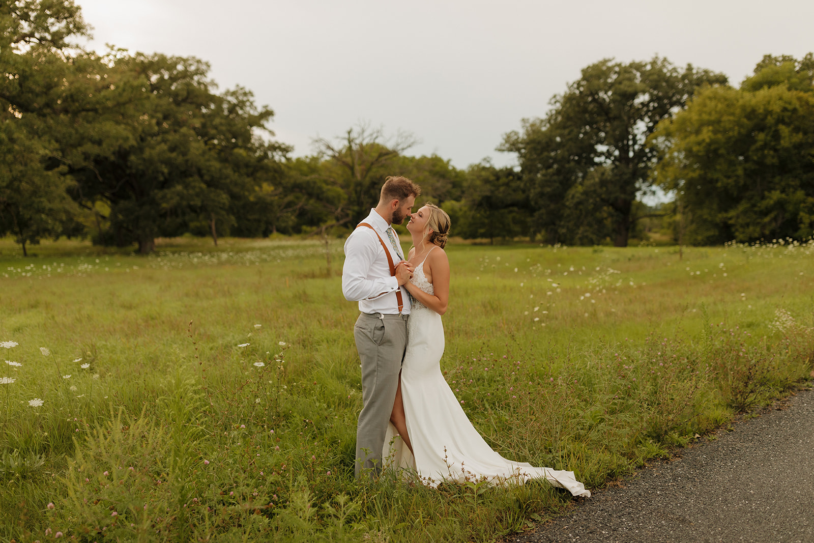 Newly married couple embracing in tall grassy field 
