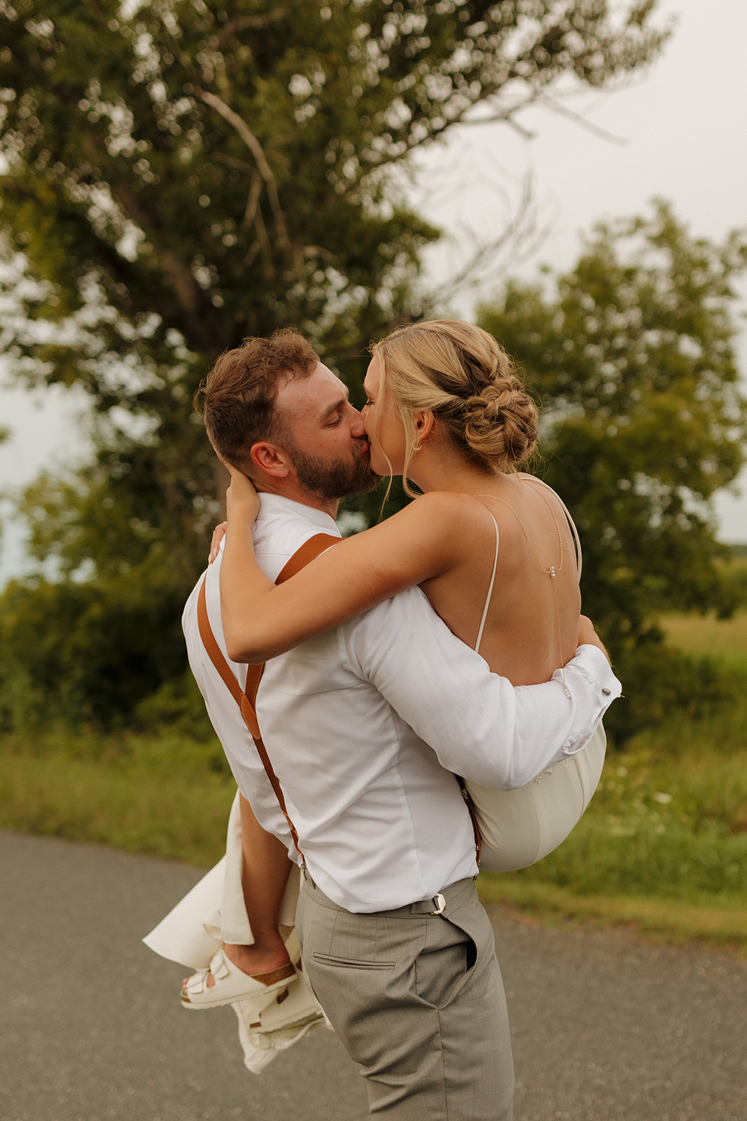 Groom lifts the bride up and carries her while kissing her romantically during outdoor portraits