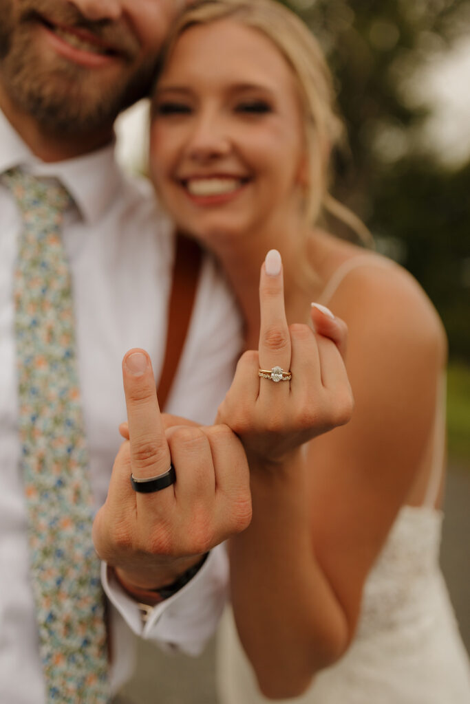 Newly married couple sticking up ring fingers showing off wedding rings, such fun outdoor wedding ideas for bridal portraits