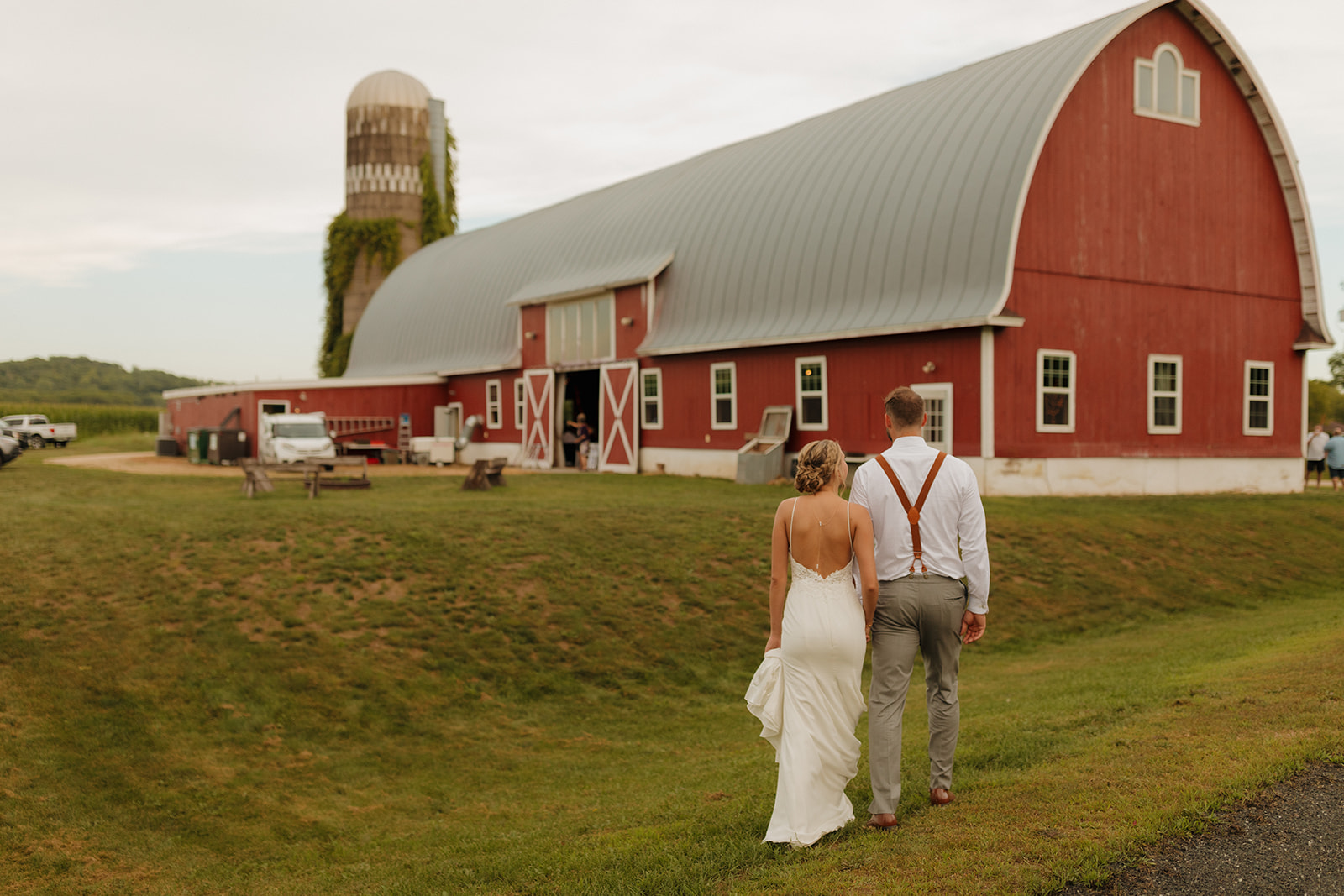 Newly married couple in wedding attire walking towards red barn as part of their outdoor wedding ideas inspiration