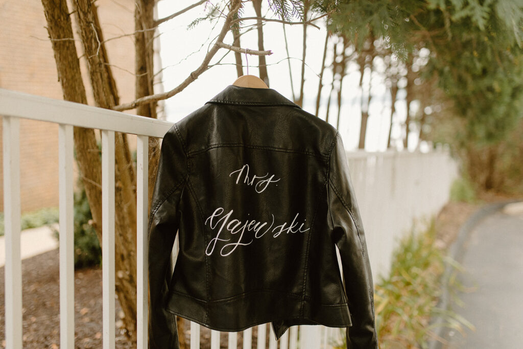 Custom black leather jacket with "Mrs. Majewski" hand-lettered on the back, hanging near trees by Lake Geneva