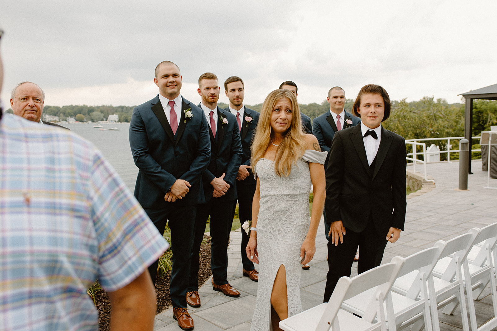 Wedding guests standing and smiling as the ceremony begins by the water
