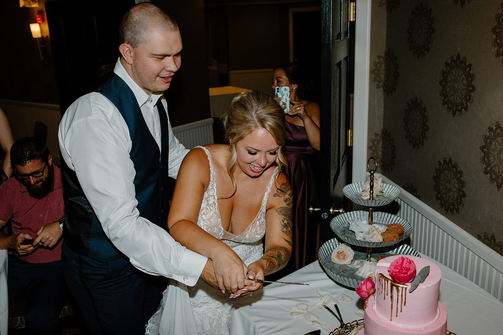 Bride and groom cutting their pink wedding cake together, laughing in the moment

