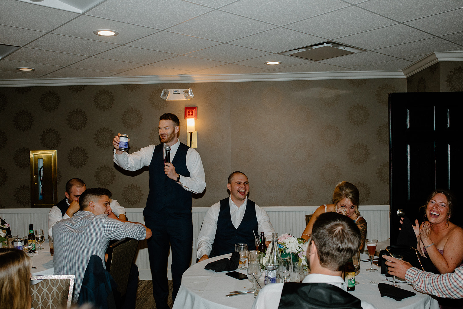 Best man raising a toast as the room erupts in laughter at the Lake Geneva wedding reception