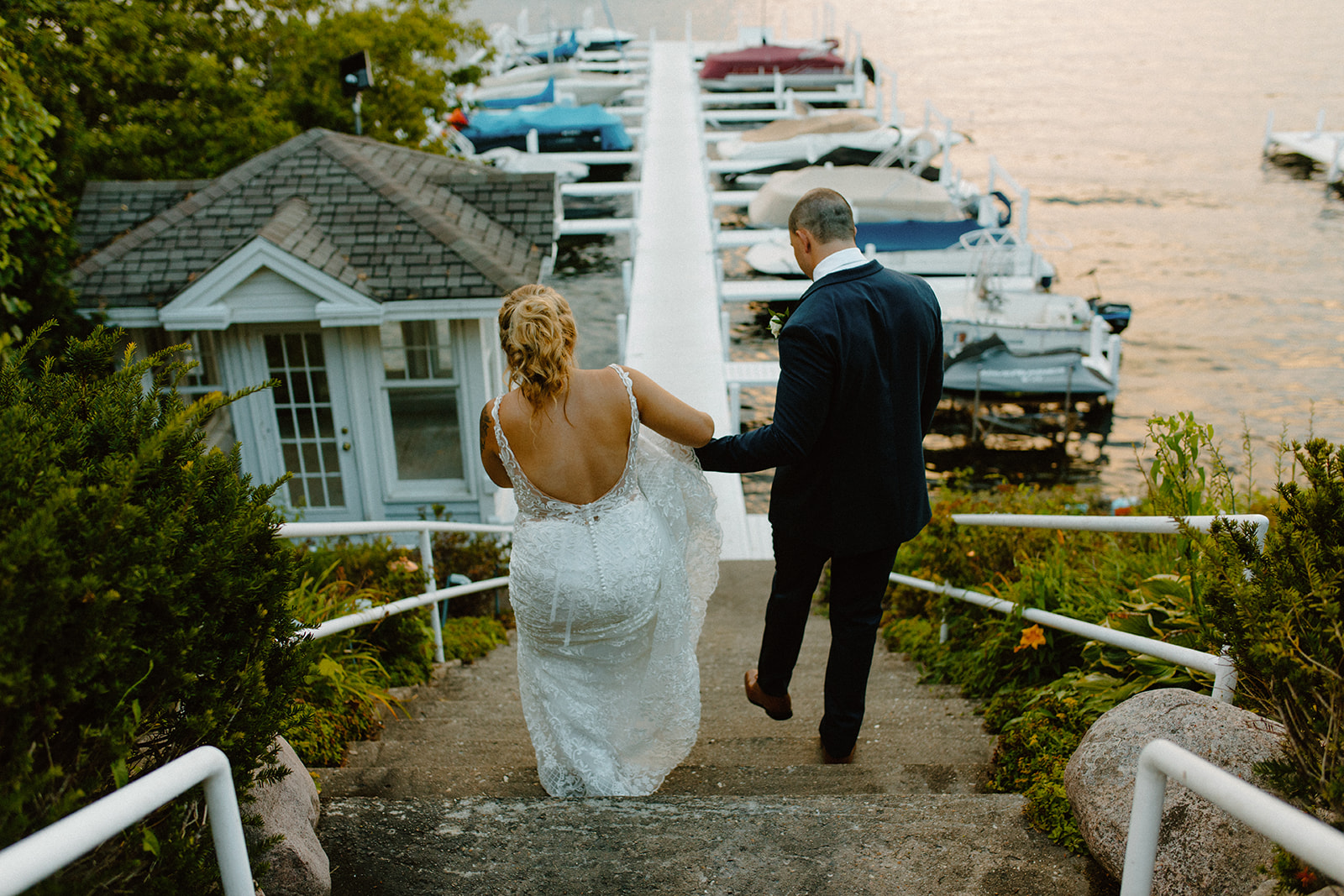 Bride and groom walking down a stone staircase toward the dock at golden hour