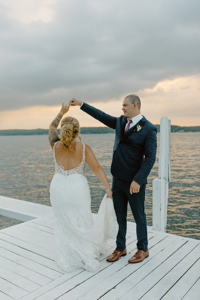 Groom twirling the bride on a white dock at sunset during their Lake Geneva wedding