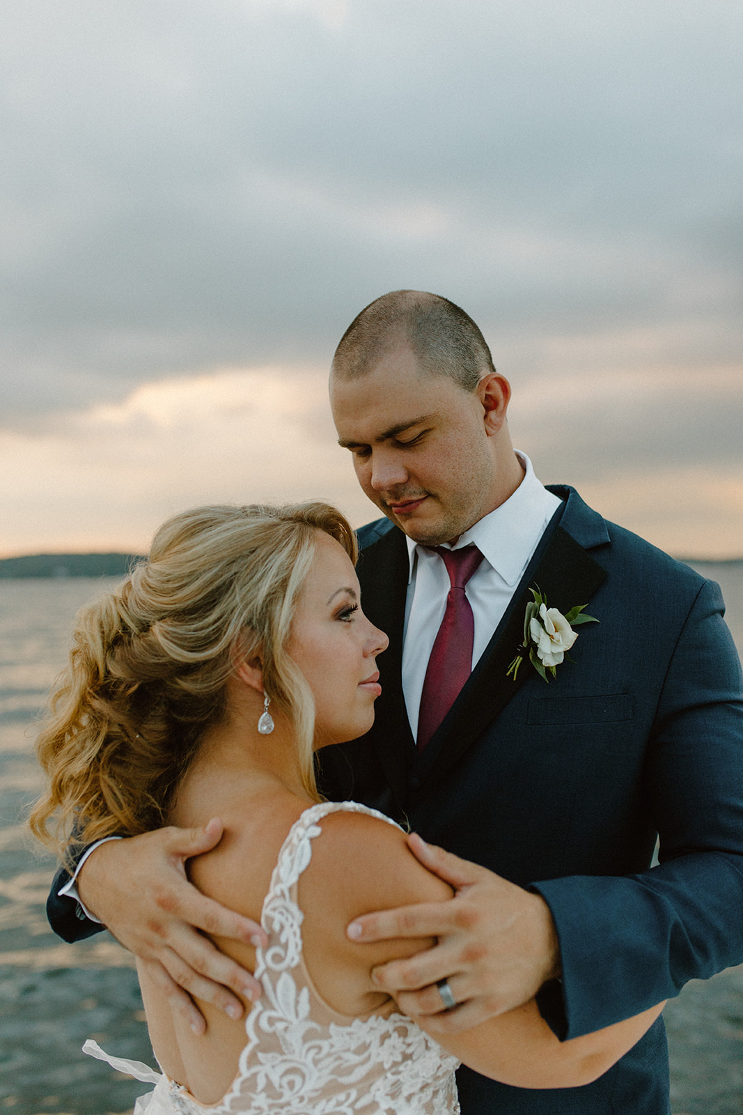 Close up of bride and groom embracing while groom looks at bride while standing on dock outside the Geneva Inn together