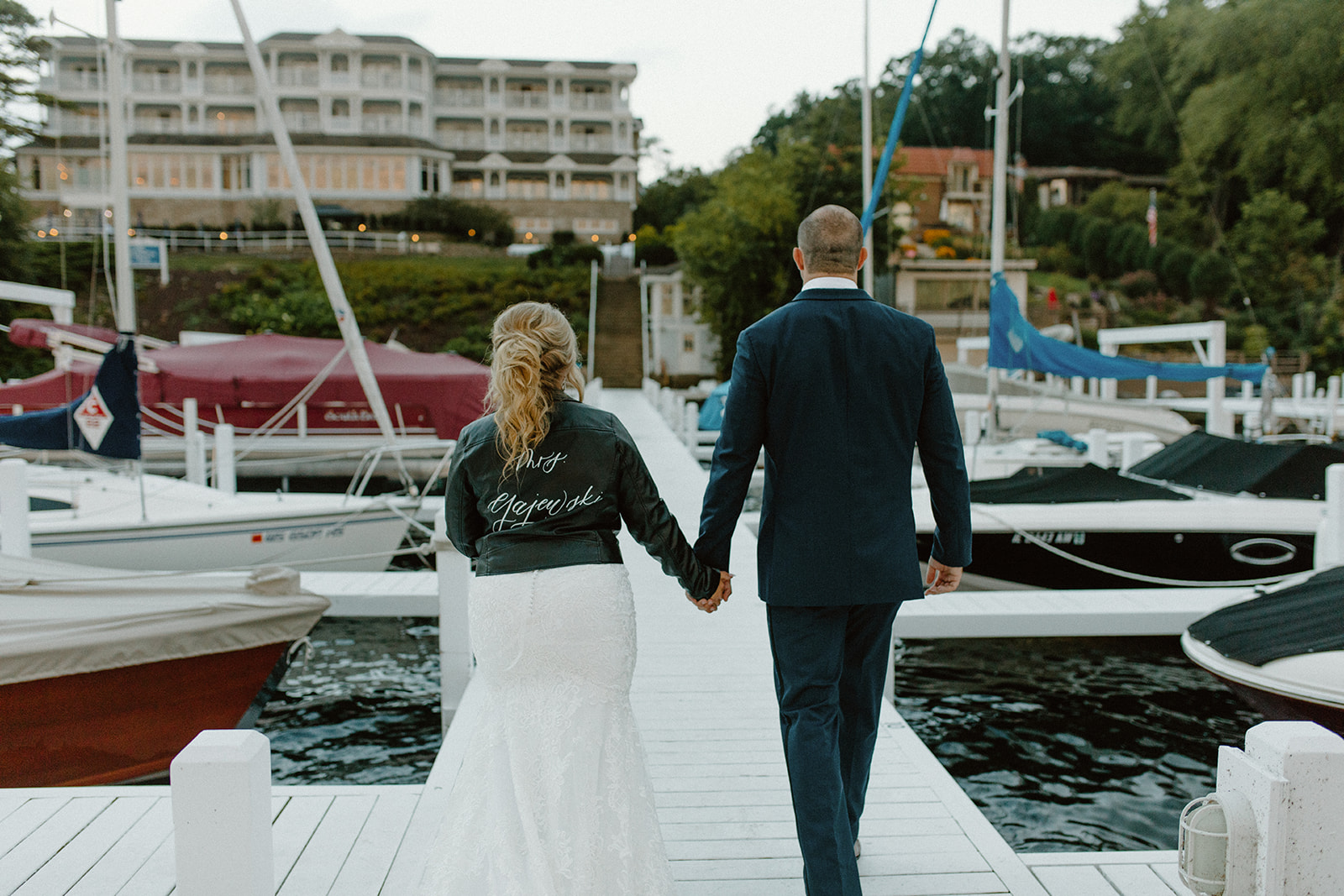 Newlyweds walk hand-in-hand down a dock with boats on either side after their Lake Geneva wedding