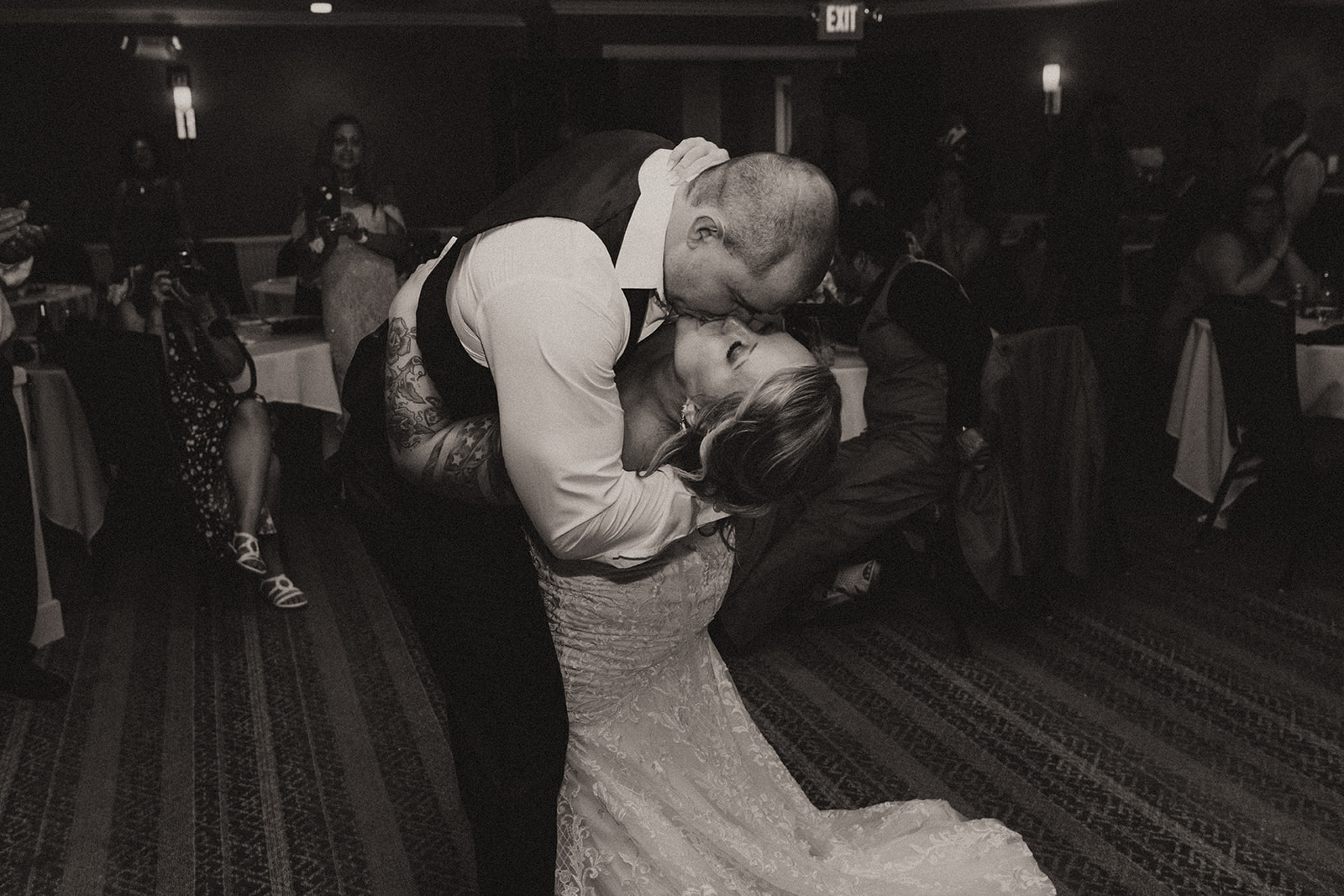 Groom dips bride for a kiss during their first dance, captured in romantic black and white