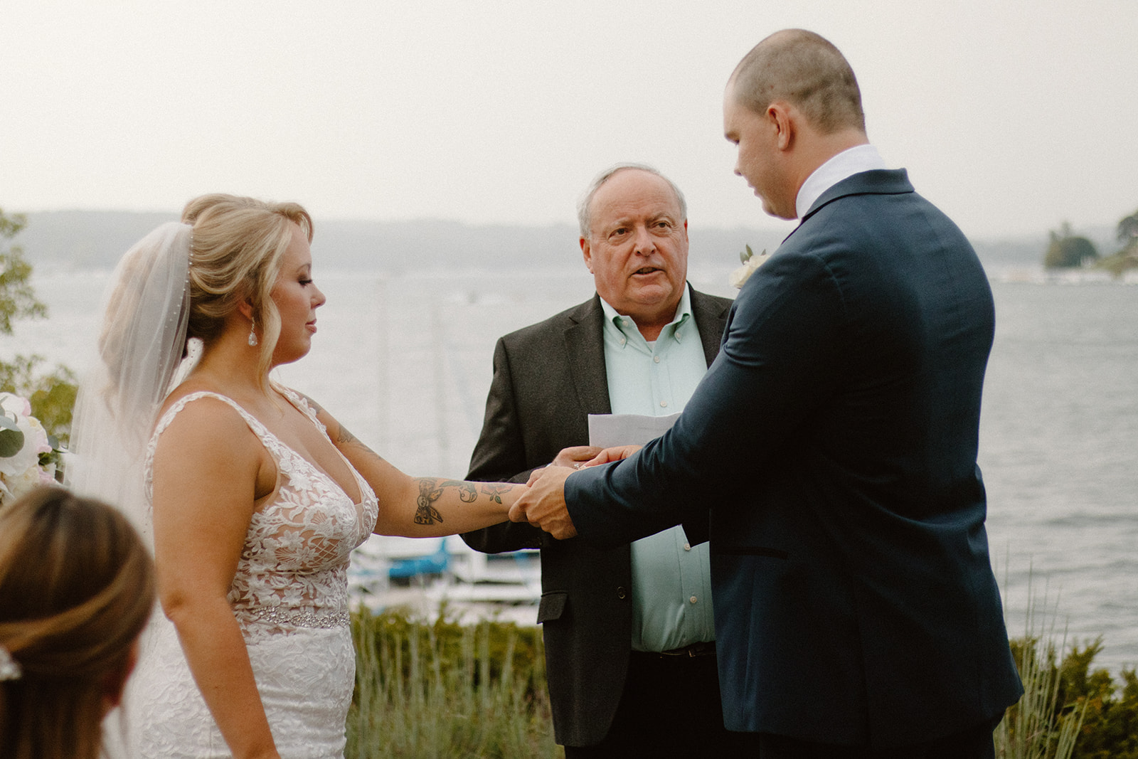 Groom placing ring on bride’s finger during a heartfelt outdoor ceremony by the lake