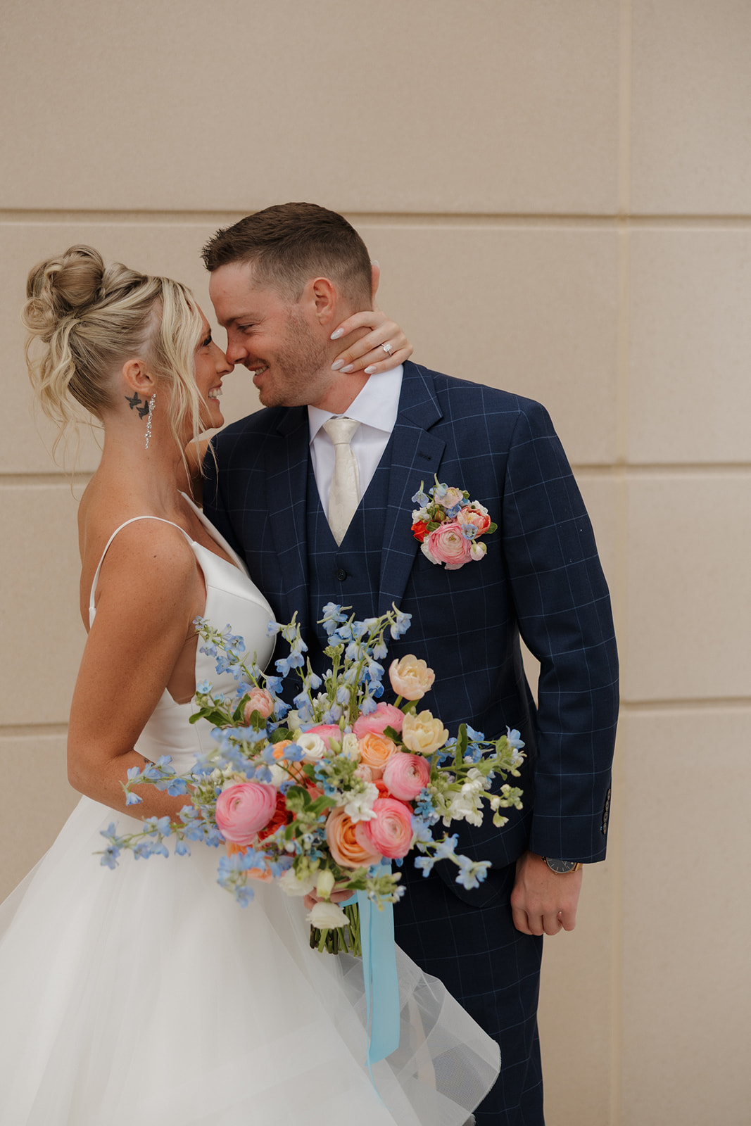 Bride and groom share a quiet moment together, bride holding a vibrant bouquet of pink, peach, and blue blooms.