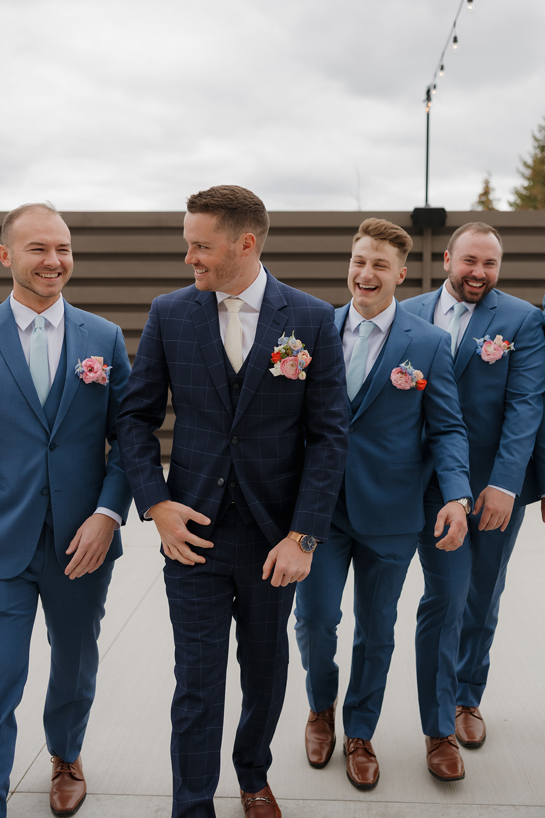 Groom walks confidently with his groomsmen in sharp blue suits, laughing together before the ceremony.