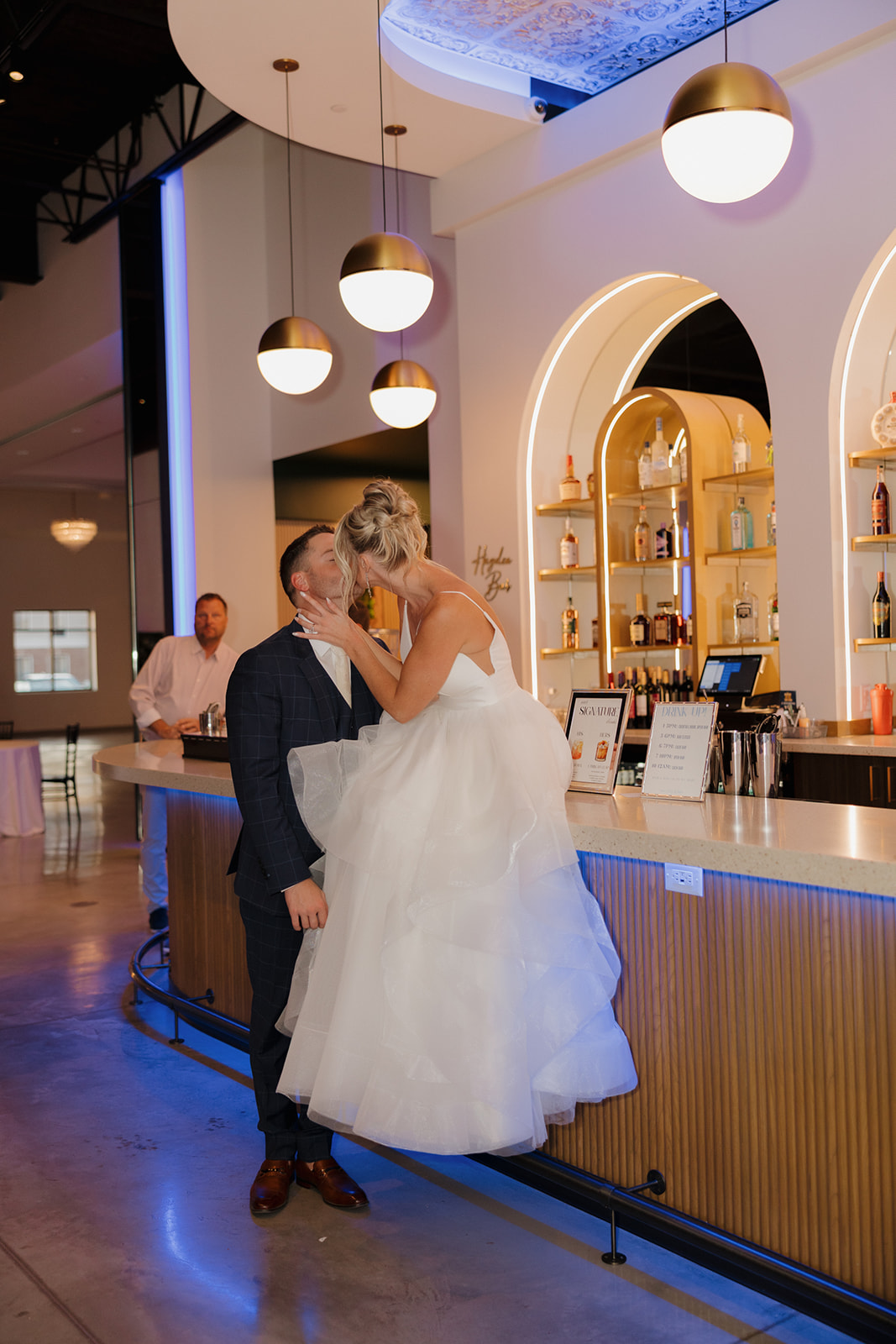 Bride perched on the bar, pulling groom in for a kiss—playful and romantic wedding moment captured in Madison, Wisconsin