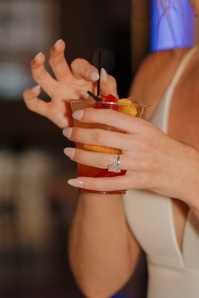 Close-up of the bride’s hand holding a cherry-garnished cocktail, with her diamond ring sparkling at her Madison Wisconsin wedding.