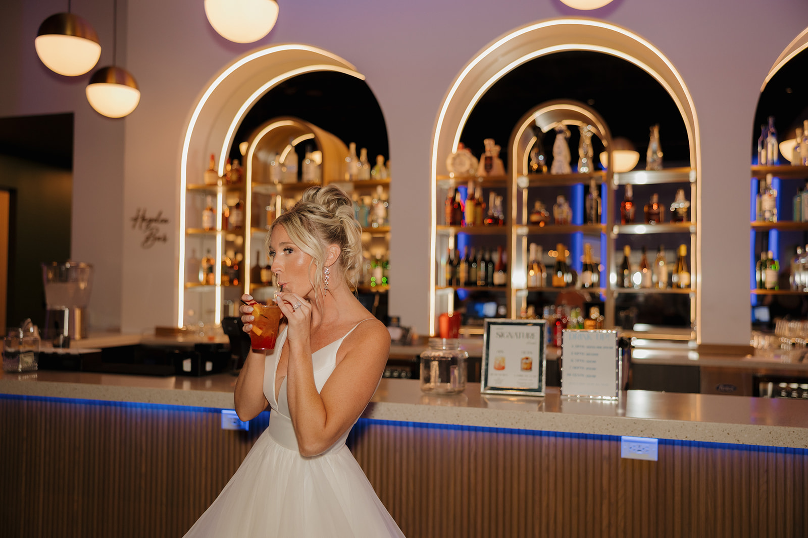 Bride sipping a signature cocktail at a glam wedding bar with glowing arches in Madison, Wisconsin.