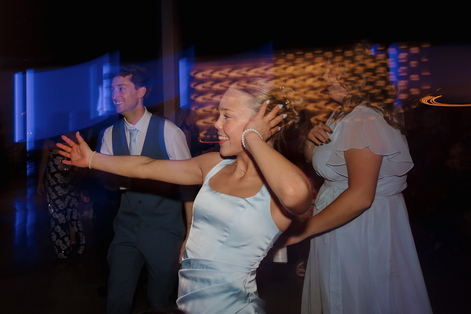 Bridesmaid dances with arms raised under colorful lights at a high-energy wedding party.