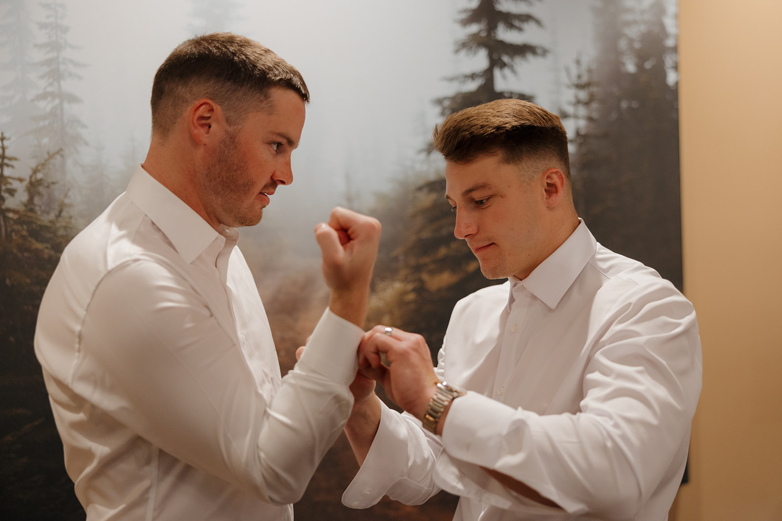 Groom and groomsman share a quiet moment while buttoning cuffs during wedding day prep.

