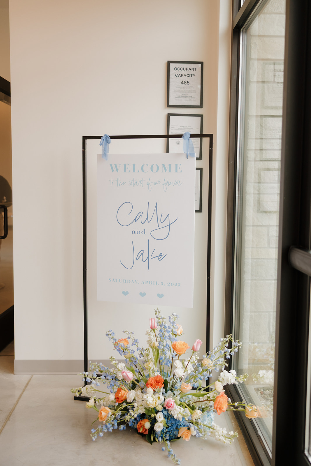 Welcome sign for Cally and Jake's wedding with spring florals at the entrance of a Madison Wisconsin wedding venue.