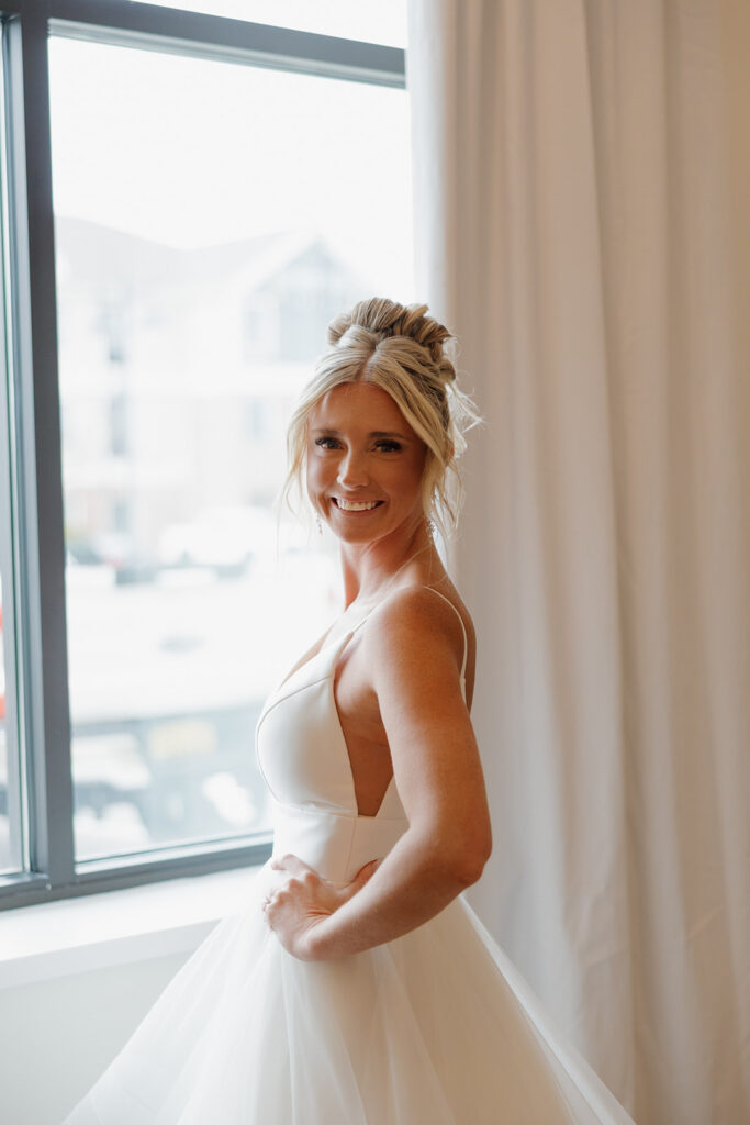 Bride glows in soft natural light while posing near a window before her Madison Wisconsin wedding ceremony. 