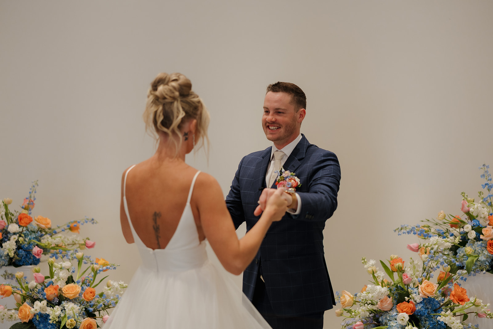 Groom beams as he sees his bride for the first time, surrounded by bright floral arrangements at their Madison Wisconsin wedding