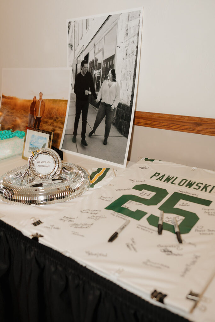 Guest book table at a country club wedding featuring a signed sports jersey and engagement photos of the couple.