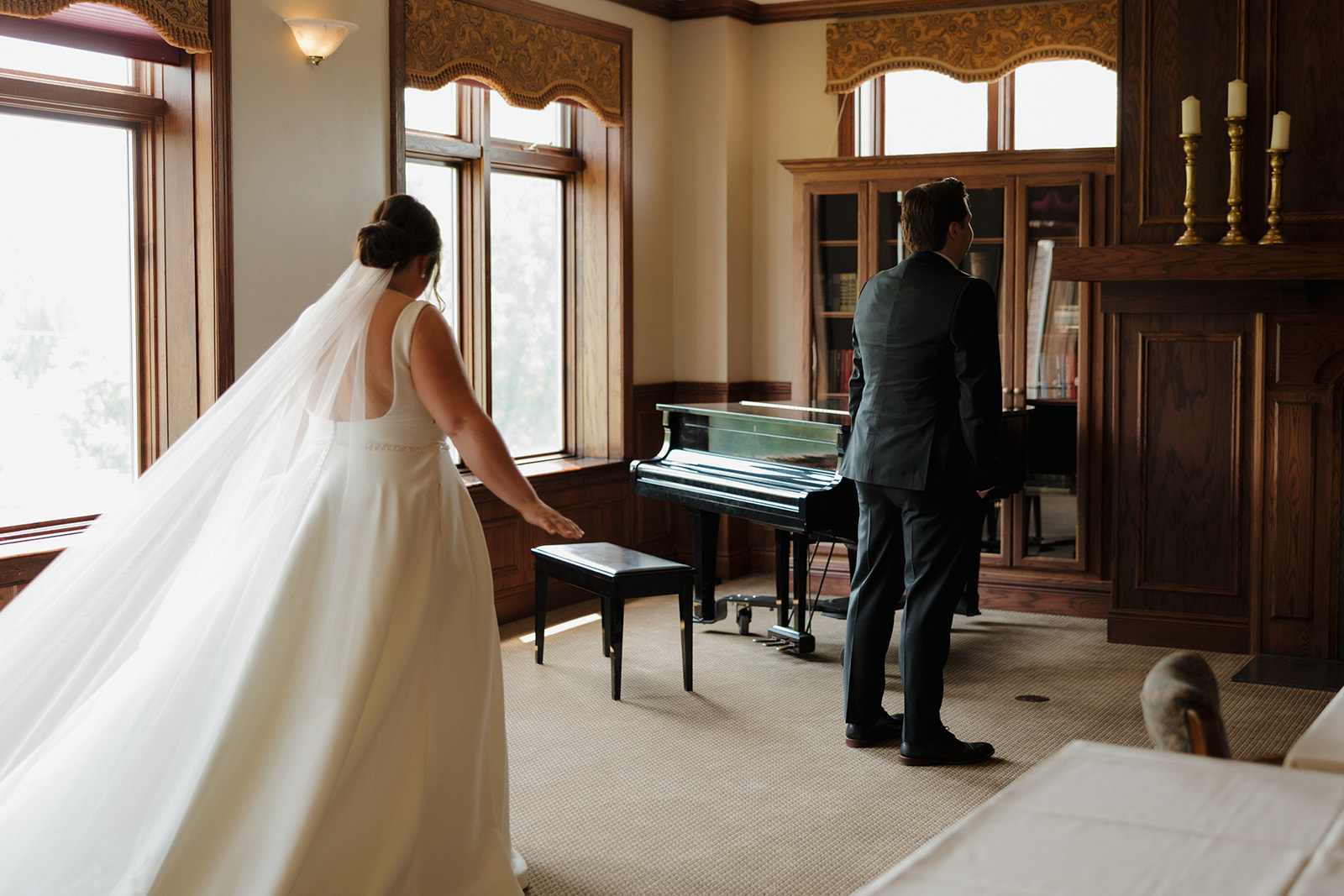 Bride walking toward her groom during a private first look moment in a cozy, wood-paneled room at their country club wedding venue.