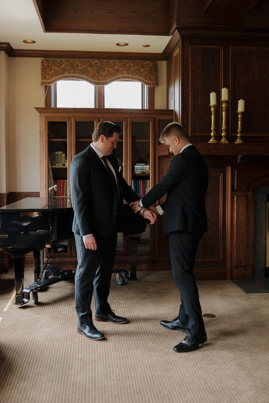 Groom adjusting his cufflinks with help from his best man in a sophisticated library room at their country club wedding venue.