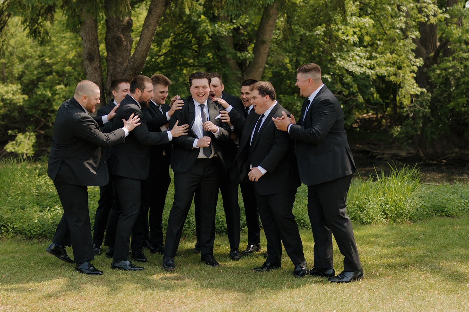 Groom surrounded by his groomsmen, all laughing and joking outdoors before the ceremony at a country club wedding.