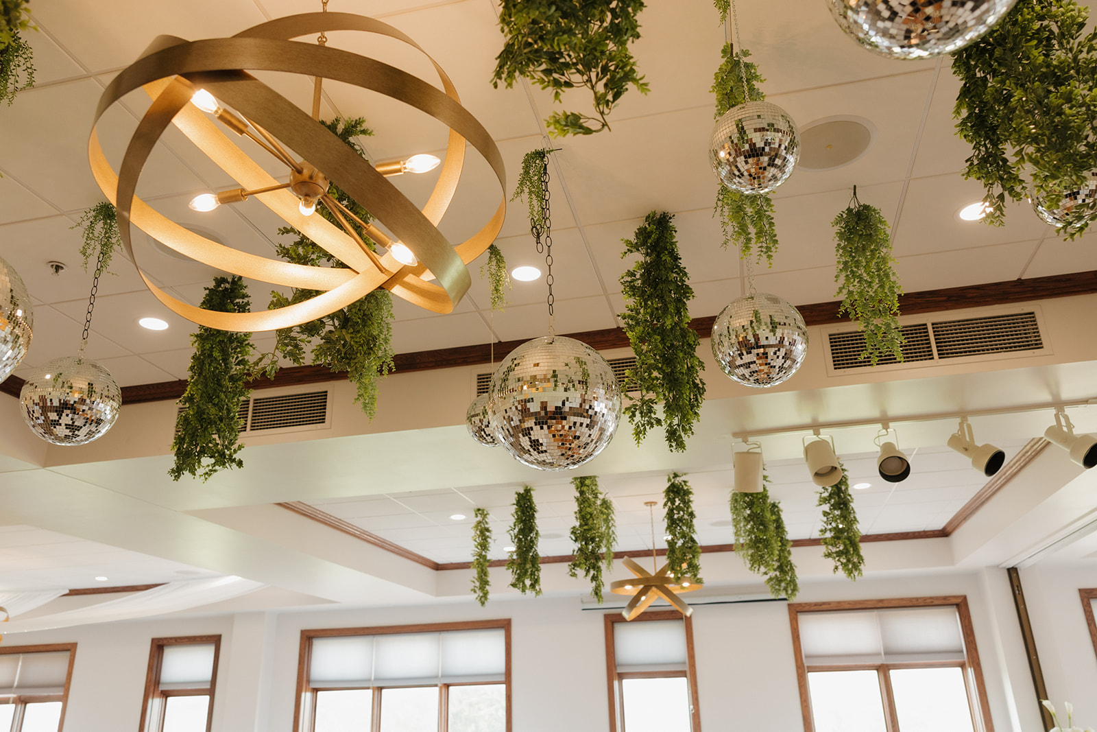 Ceiling decor at a country club wedding reception featuring hanging greenery, metallic light fixtures, and mirrored disco balls for a fun, modern vibe.