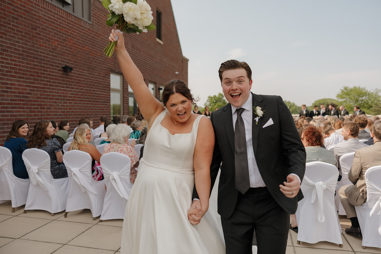 Bride and groom celebrating down the aisle after saying “I do” at their outdoor country club wedding ceremony, with the bride raising her bouquet in joy.