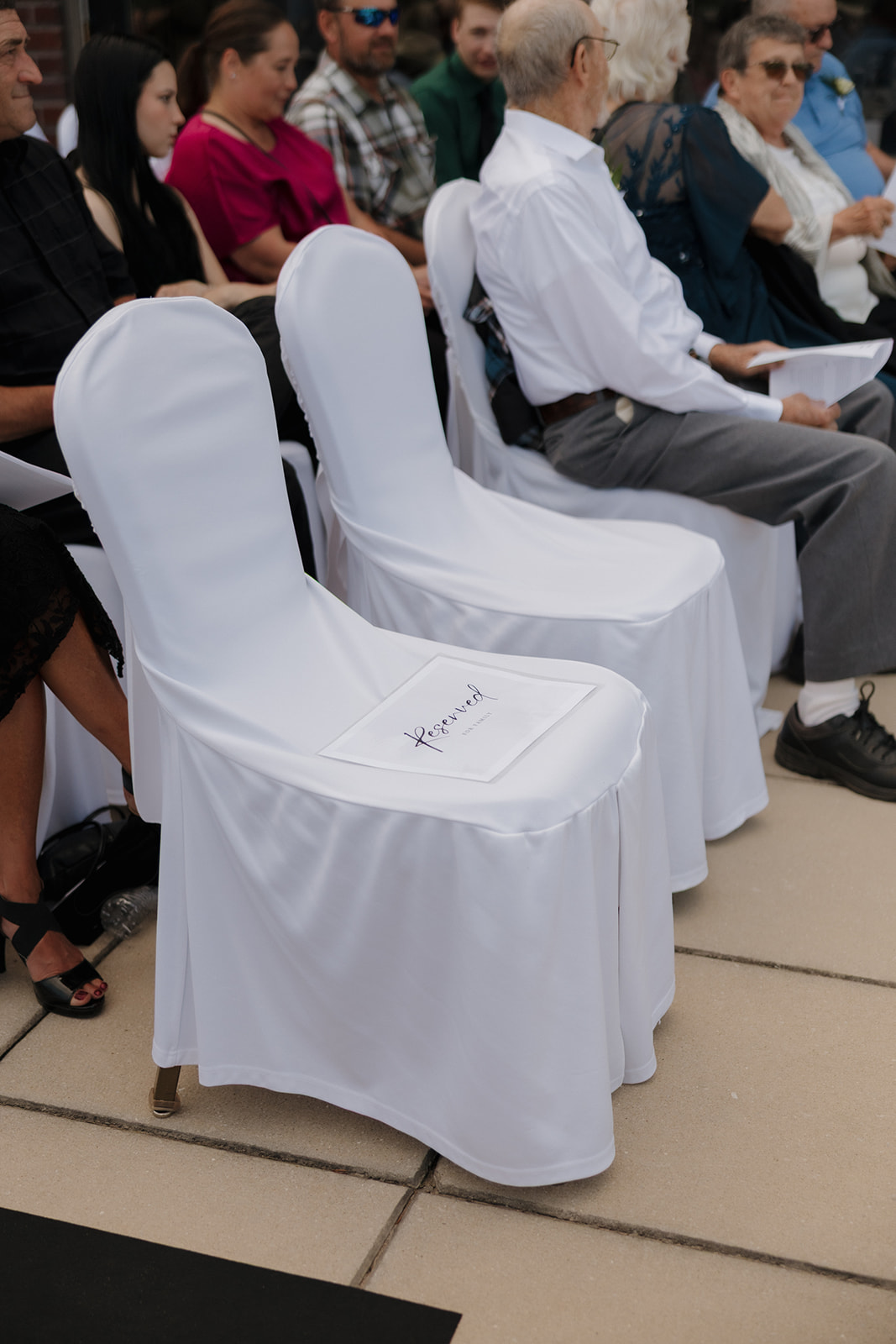 White chair with a “Reserved” sign at an outdoor country club wedding ceremony, surrounded by seated guests waiting for the celebration to begin.