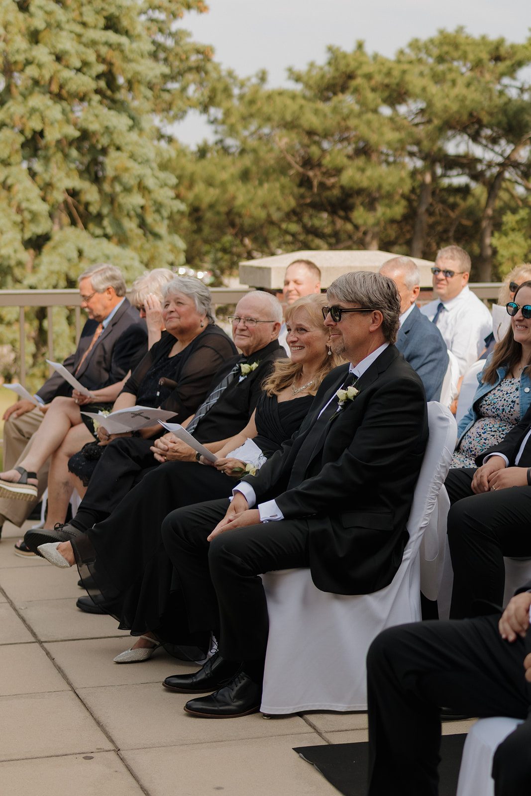 Guests seated at a country club wedding ceremony, including parents smiling proudly as they watch the couple exchange vows.