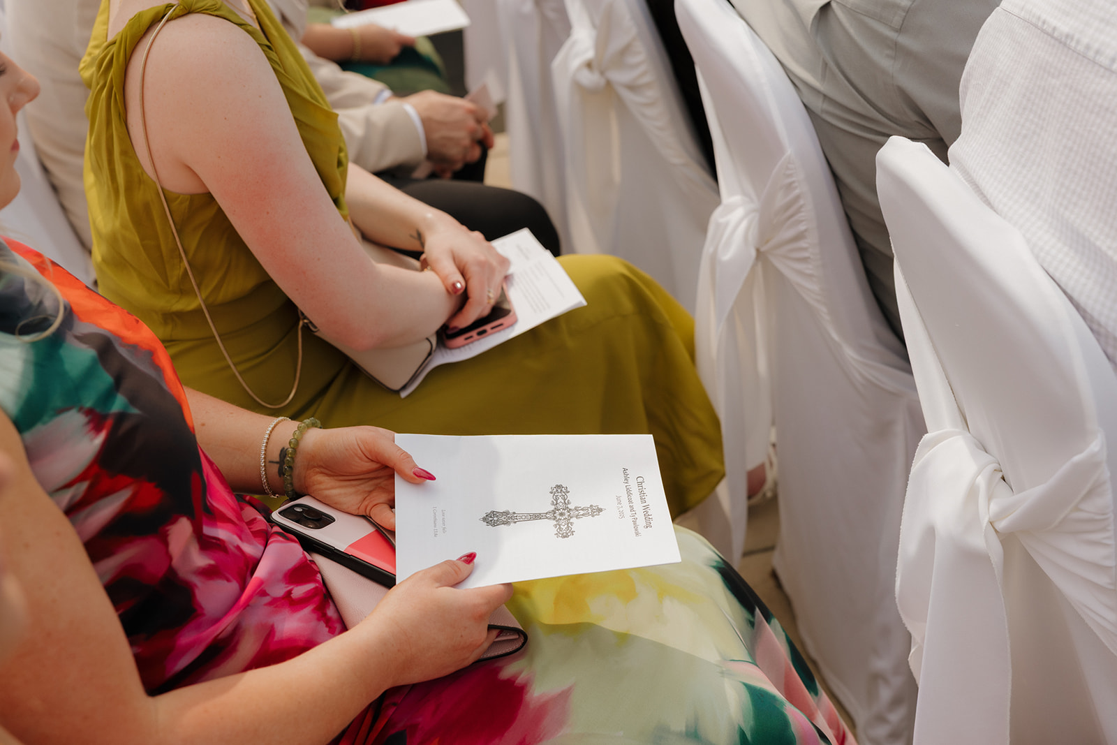 Close-up of a guest holding the printed wedding ceremony program while seated among rows of white chair covers at a country club wedding.