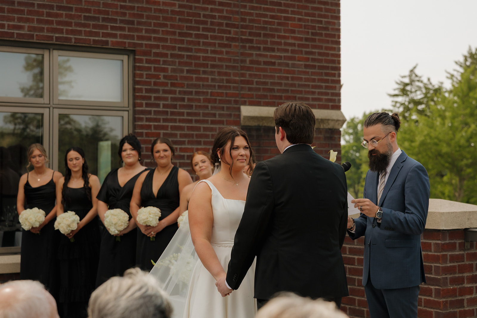 Bride and groom exchanging vows while the bridesmaids stand nearby, framed by the red brick walls of the country club ceremony patio.