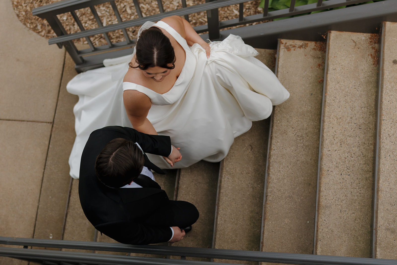 Overhead shot of the bride holding her dress while walking up the stairs with the groom during a country club wedding day.